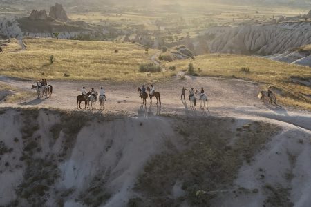 Group riding horses through Cappadocia valleys at sunset