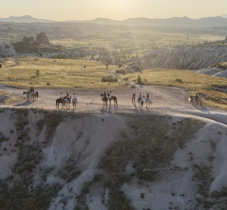 Group riding horses through Cappadocia valleys at sunset