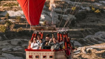 Hot air balloon with passengers flying over Cappadocia landscape.