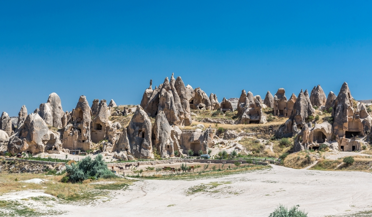 A panoramic view of Cappadocia’s famous fairy chimneys and cave houses carved into volcanic rock. The image highlights the historic cave dwellings scattered among the striking natural rock formations, set against a vivid blue sky.