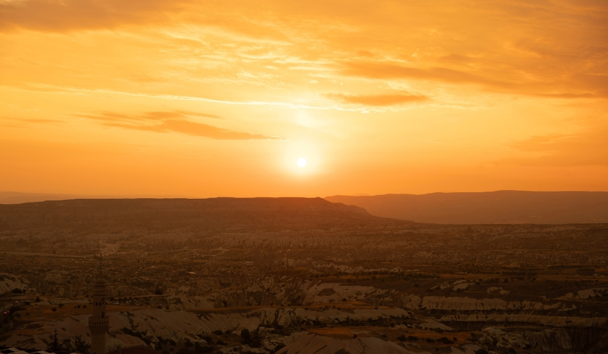 A stunning view of the sun setting over Cappadocia’s valleys, with the landscape bathed in warm golden light. The scene highlights the magical atmosphere that makes sunrise and sunset in Cappadocia one of the most iconic experiences for travelers.